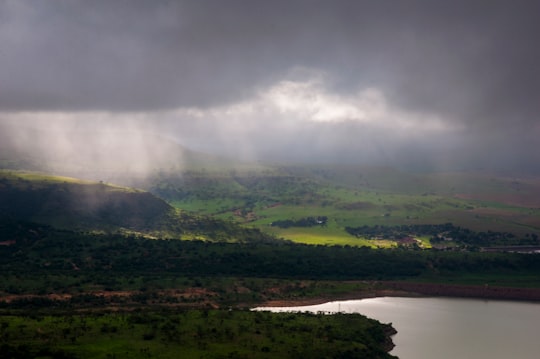 green trees near body of water under white clouds during daytime in Drakensberg South Africa