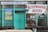 A building facade with a teal green color scheme, featuring a sign in Cyrillic script indicating a veterinary pharmacy. The entrance has a glass window and a wooden door. Posters with various animals, including a cow and dog, decorate the exterior.