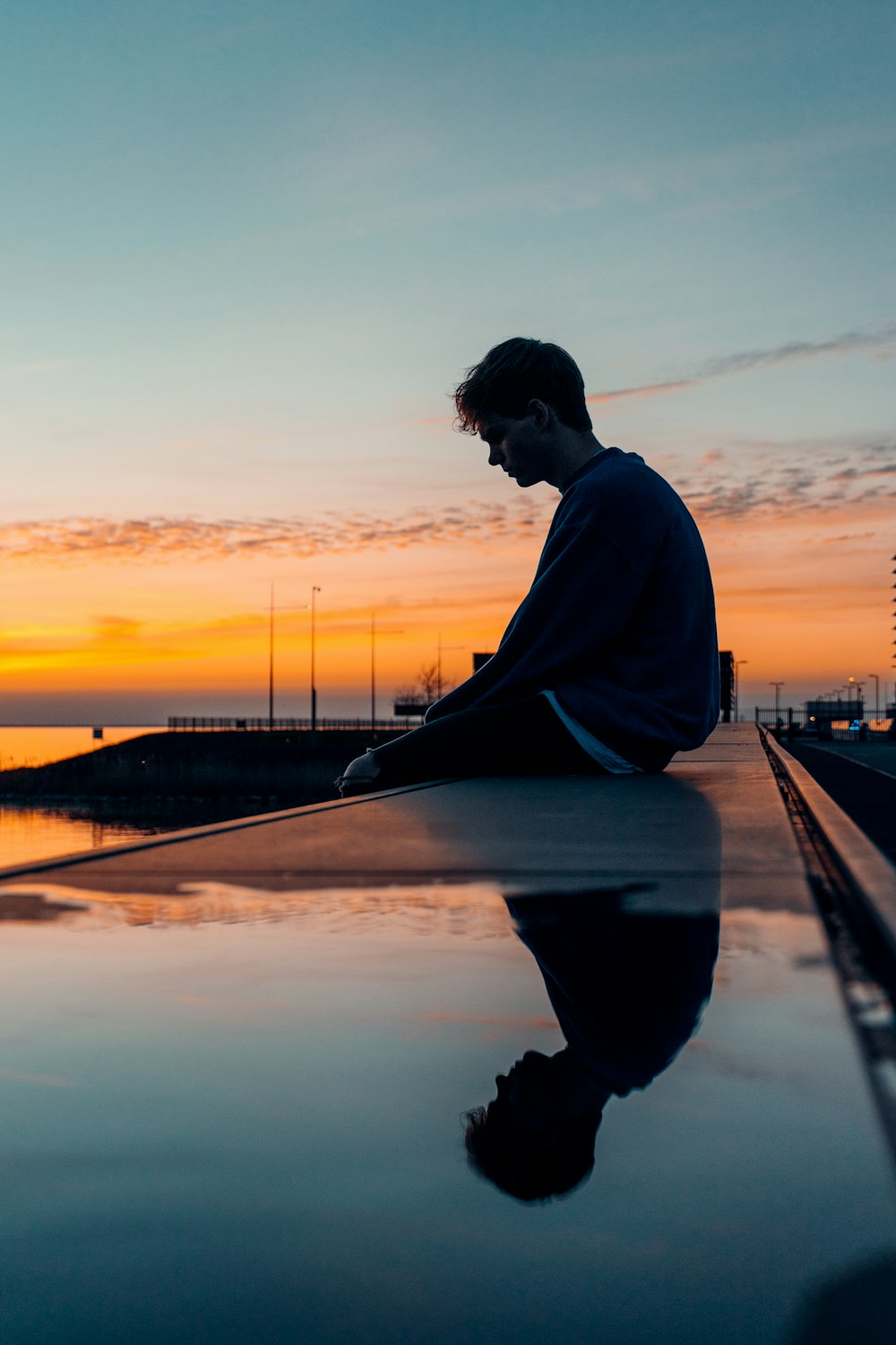 man in white long sleeve shirt and black pants sitting on dock during sunset