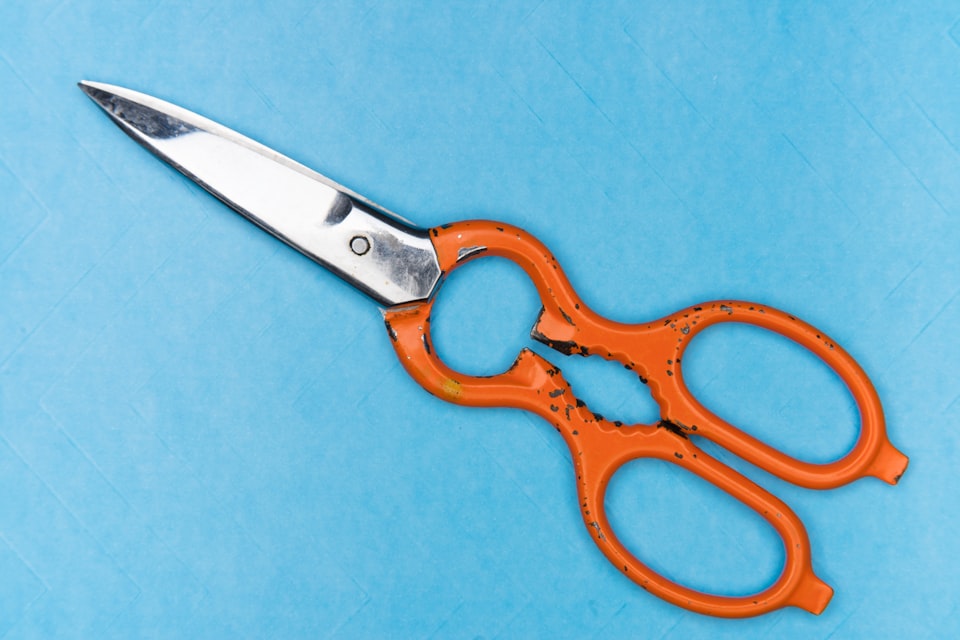 Orange handled scissors on a sky blue background