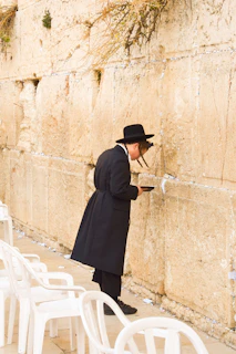 woman in black coat and black skirt standing beside brown concrete wall during daytime