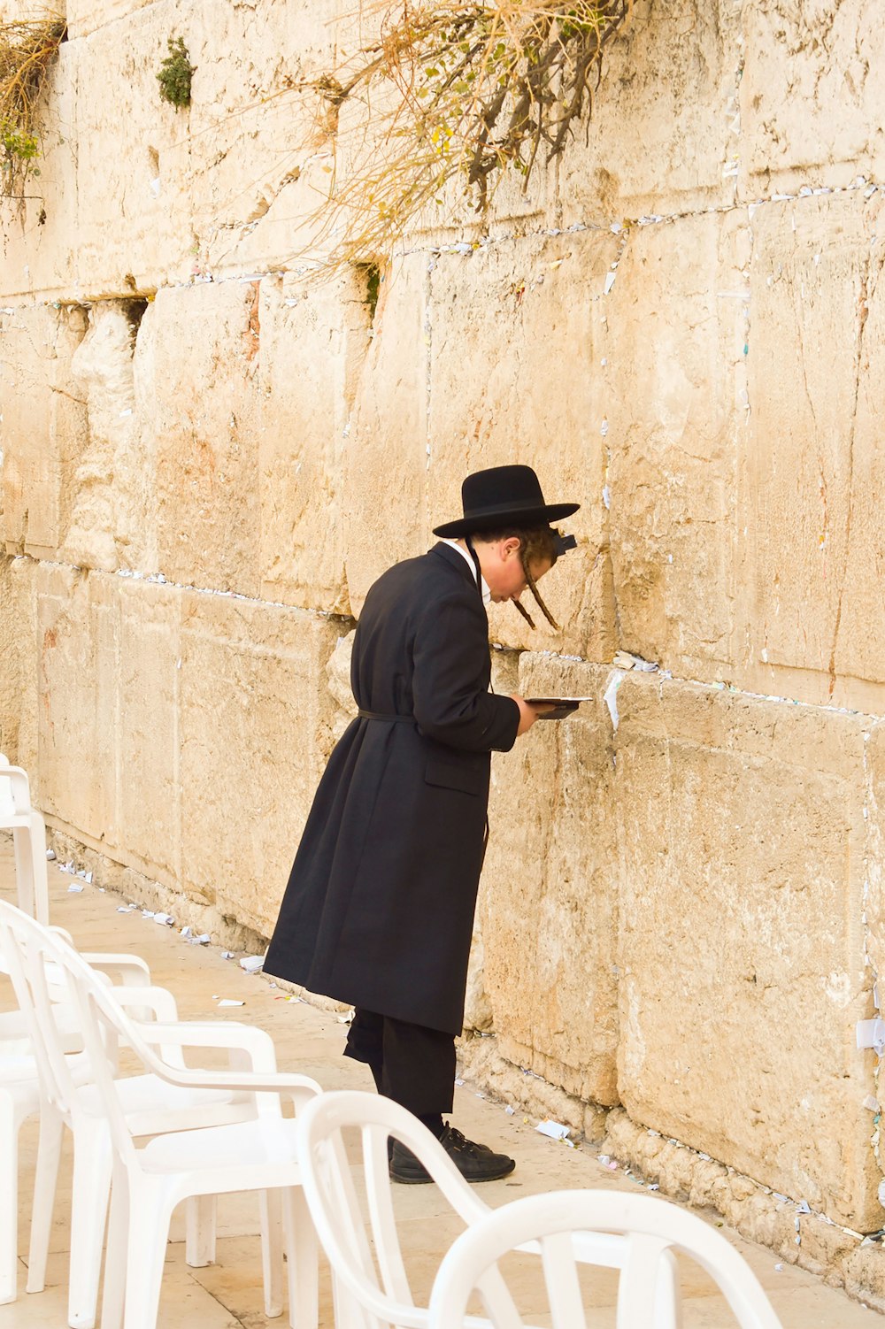 woman in black coat and black skirt standing beside brown concrete wall during daytime