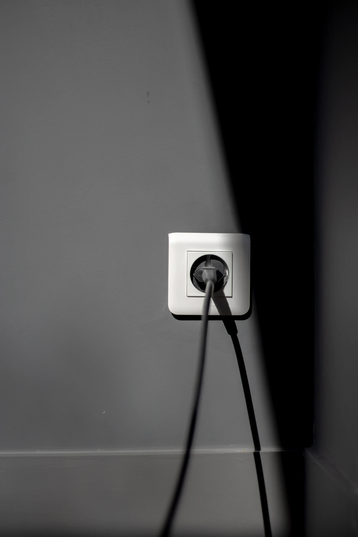 Čierna elektrická zástrčka zapojená do bielej zásuvky