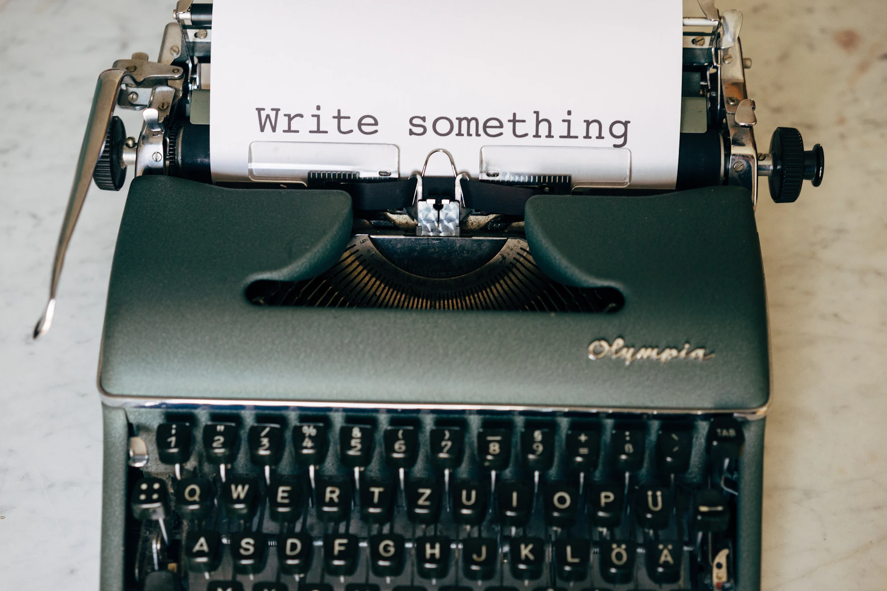 A gray-green manual typewriter seen from the front, with the words Write something typed on the loaded page