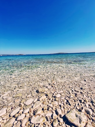 A peaceful Danish coastline with smooth pebbles and calm blue waters under a clear sky.