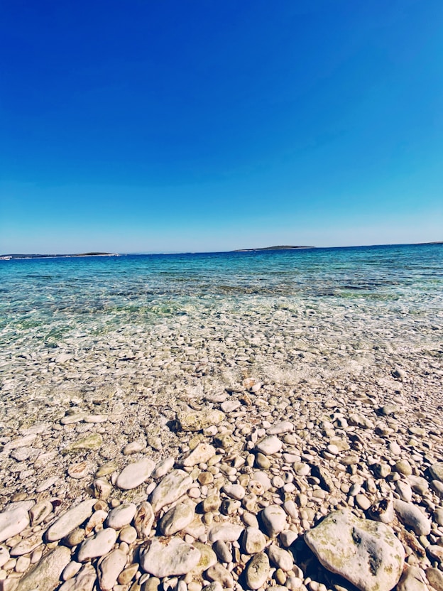 A peaceful Danish coastline with smooth pebbles and calm blue waters under a clear sky.