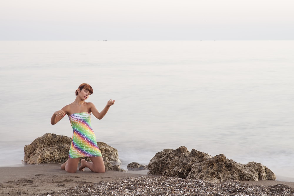 girl in pink and white floral swimsuit sitting on rock near sea during daytime