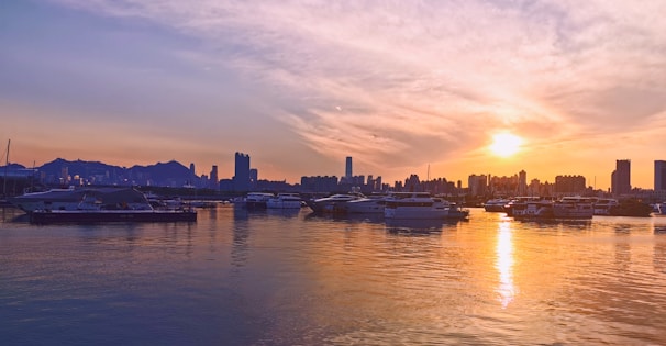 A serene view of the Hong Kong skyline at sunset, with boats gently floating on the harbor.