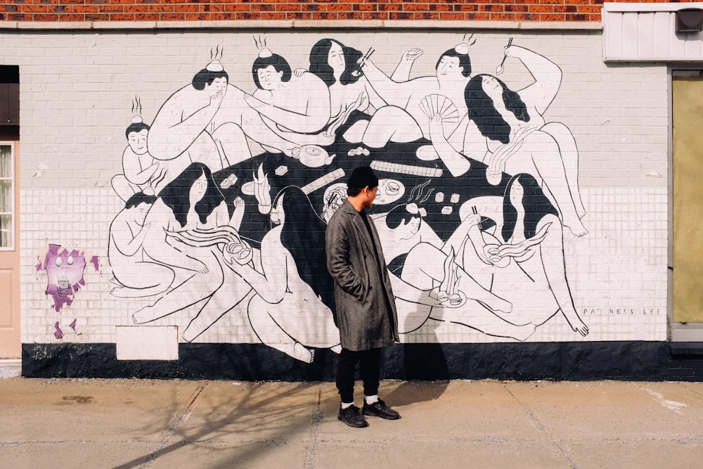Personne vêtue d’un manteau gris debout devant un mur avec des graffitis