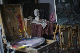 An artist's studio corner with brushes, paints, and a canvas in progress.