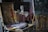 An artist's studio filled with various painting equipment including a palette with paint, brushes, and easels. A painted canvas is placed on one easel, and a sculpted head bust is situated on a table covered with a cloth. The setting is cluttered, indicative of an active, creative space.