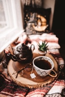 A neatly arranged wooden tray holding a warm cup of tea and a small potted plant on a clean white table.