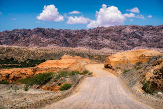 A winding dirt road cutting through vast, rugged desert landscape under a bright blue sky