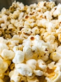 A close-up view of freshly popped corn, showcasing the fluffy and irregular shapes of the kernels. The popcorn has a light yellow and white coloration with some golden brown highlights.