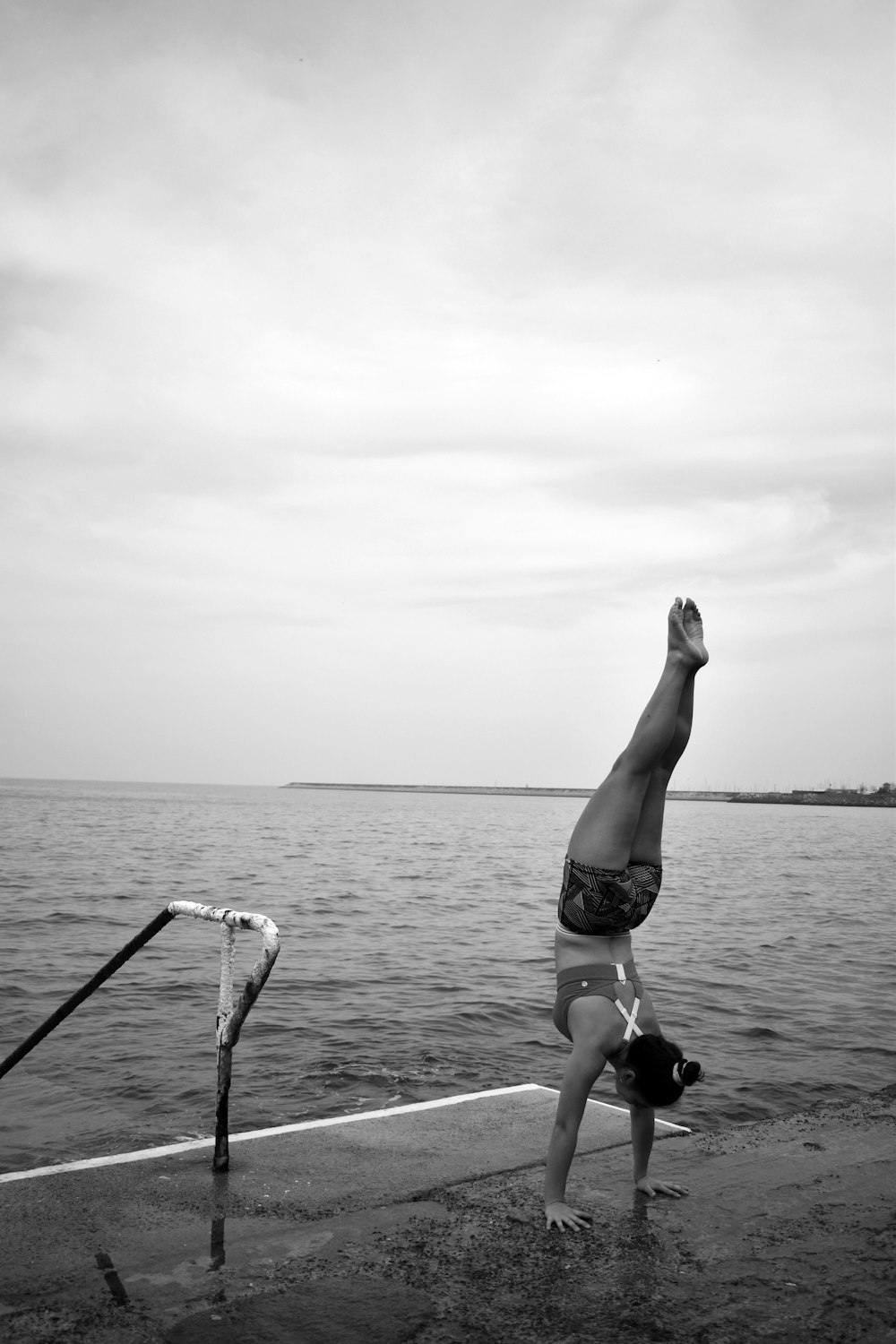 grayscale photo of woman in bikini sitting on wooden dock