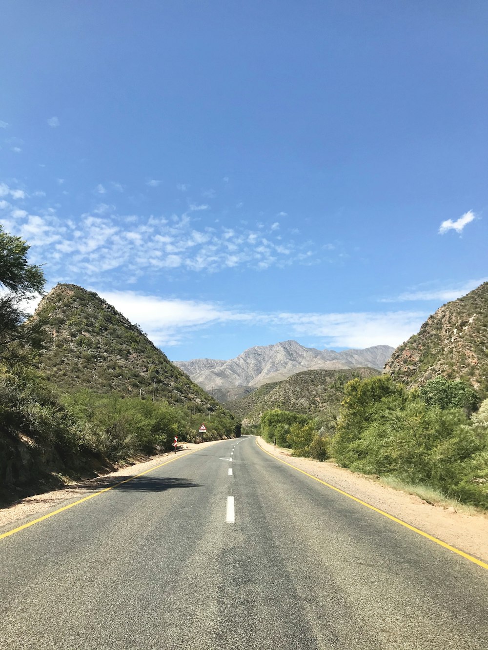 gray asphalt road near green trees and mountain under blue sky during daytime