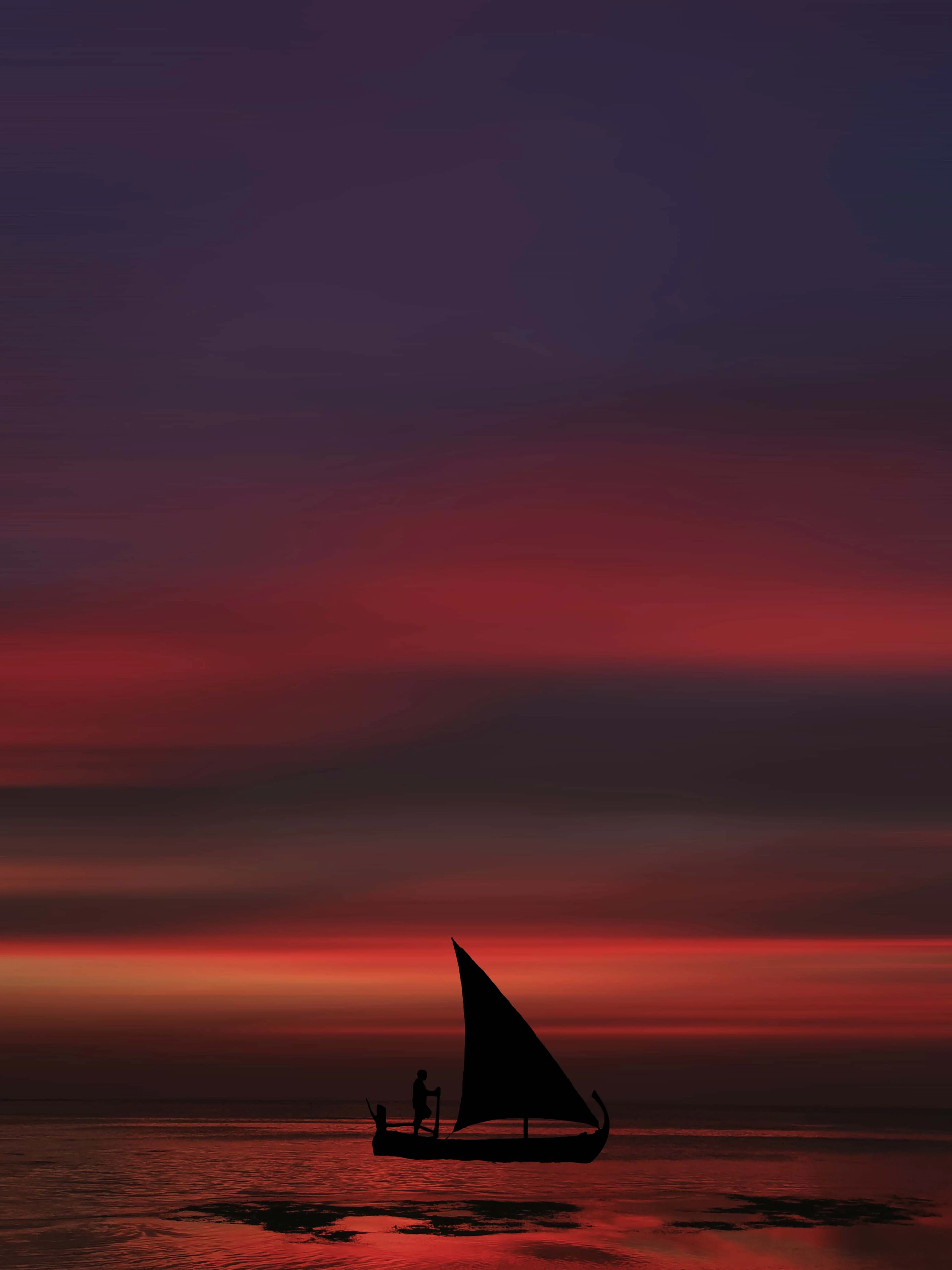 Dhow sailboat silhouette against a fiery sunset over the ocean