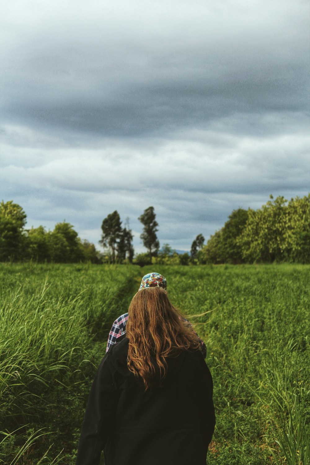 woman in black jacket sitting on green grass field under gray cloudy sky during daytime