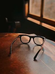 A close-up of elegant eyeglasses resting on a soft cloud-like fabric, bathed in warm sunlight.