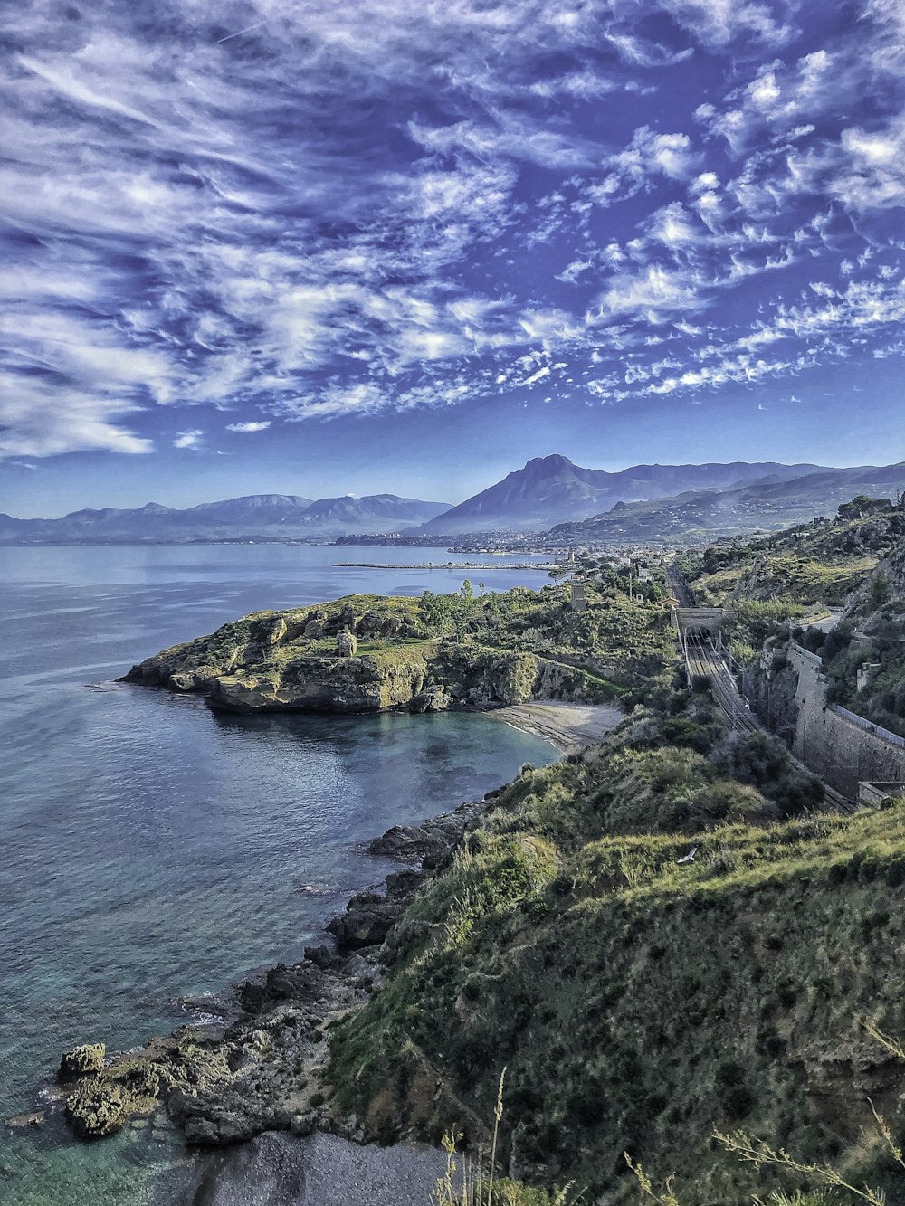 green and brown mountain beside blue sea under blue sky during daytime