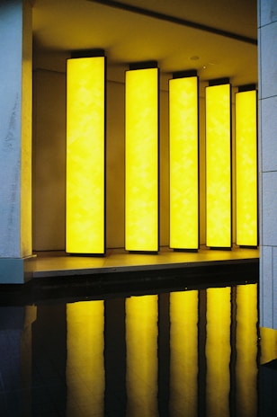 Tall, rectangular yellow light panels are vertically aligned and partially reflected in a dark, glossy surface below, creating a striking visual effect.