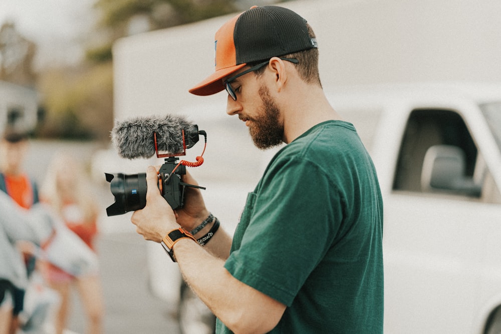 Hombre con camiseta verde de cuello redondo sosteniendo una cámara DSLR negra