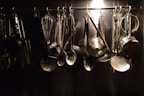 Close-up of shiny kitchen utensils including spatulas, ladles, and whisks hanging on a rack