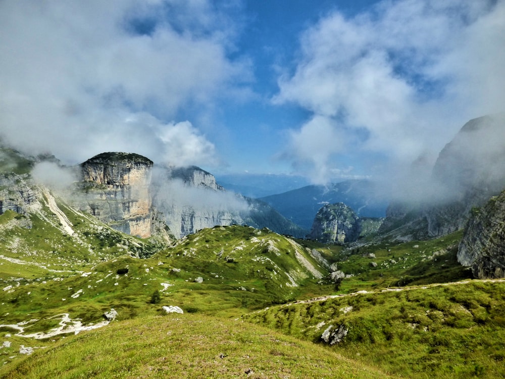 green grass field near mountain under white clouds and blue sky during daytime