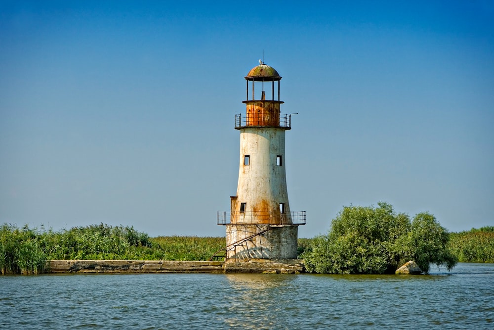 Phare blanc et brun près des arbres verts sous le ciel bleu pendant la journée