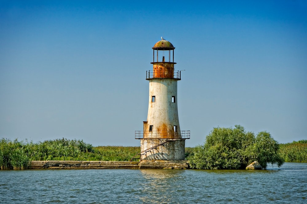white and brown lighthouse near green trees under blue sky during daytime