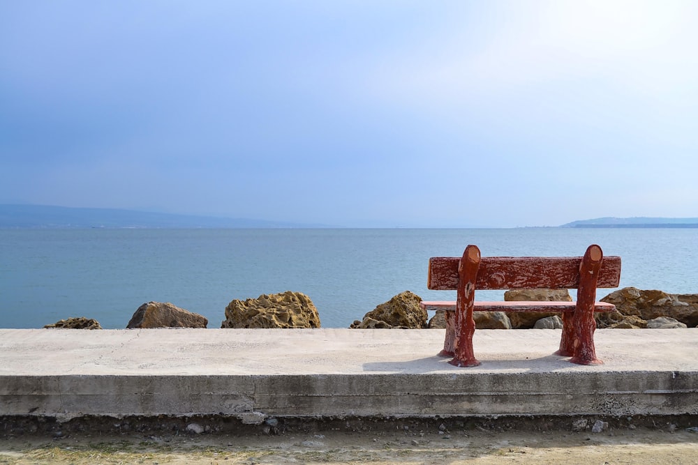 red wooden bench on gray concrete floor near body of water during daytime