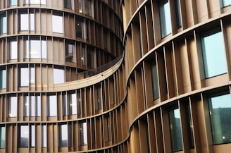 Curved architectural structure with vertical slats separating reflective glass windows. The building's facade creates an undulating pattern with a sleek and modern design.