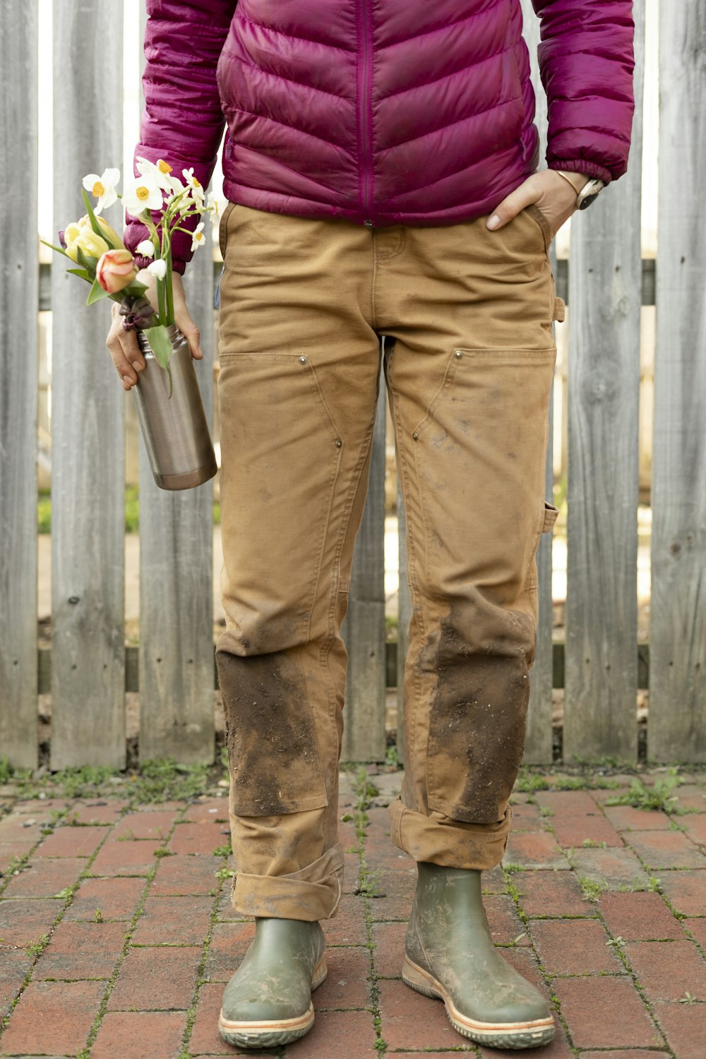 personne en pantalon marron et chemise violette tenant un bouquet de fleurs