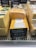 Several blocks of various cheeses are displayed in a deli case. The cheeses are wrapped in plastic with visible labels. A black sign indicates that one of the cheeses is 'Cheddar Coloured' priced at £6.60 per kilogram. Other cheeses have different prices displayed above them.