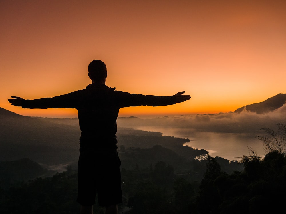 silhouette dell'uomo in piedi sulla cima della montagna durante il tramonto