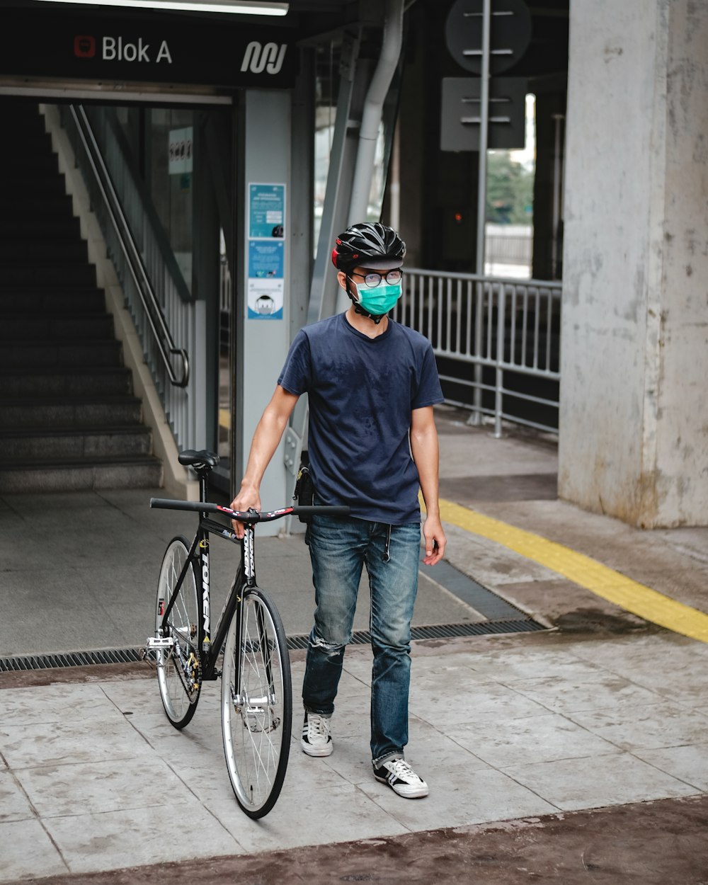 man in blue crew neck t-shirt and blue denim jeans standing beside black bicycle during