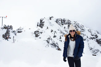 Close-up portrait of a smiling snowscoot rider in winter gear with mountains behind.