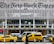 Yellow taxis are parked and driving in front of a modern building with large lettering displaying a well-known newspaper name. The facade is made up of metal slats and glass, creating a sleek and urban atmosphere. Pedestrians and various vehicles are also present in the busy city environment.