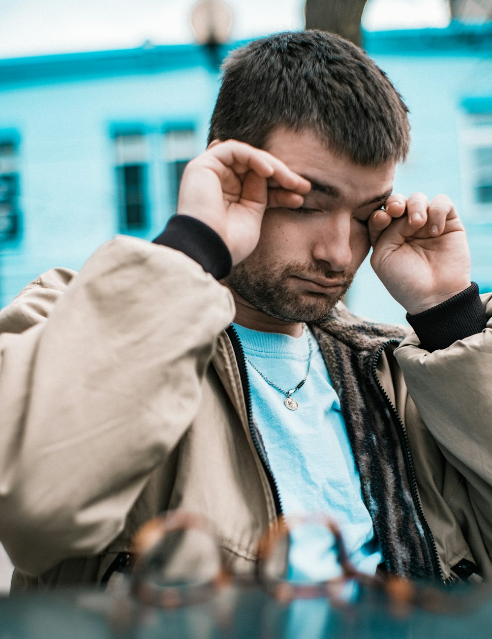 man in brown coat covering his face with his hand