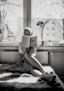A person smiling while reading a self-help book in a bright, minimalist room.