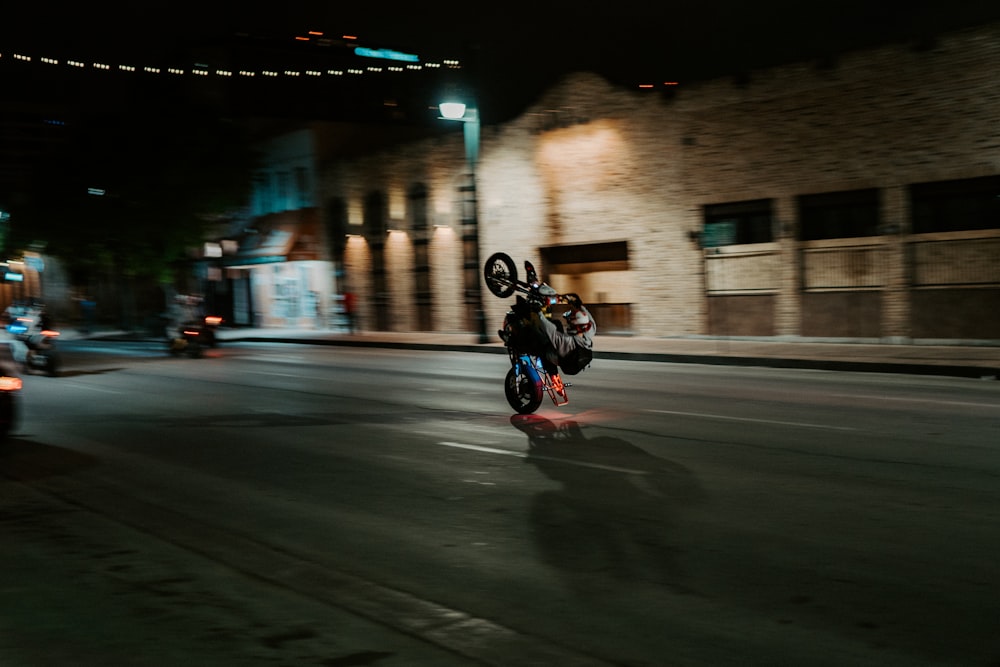 Mann in schwarzer Jacke fährt nachts Motorrad auf der Straße