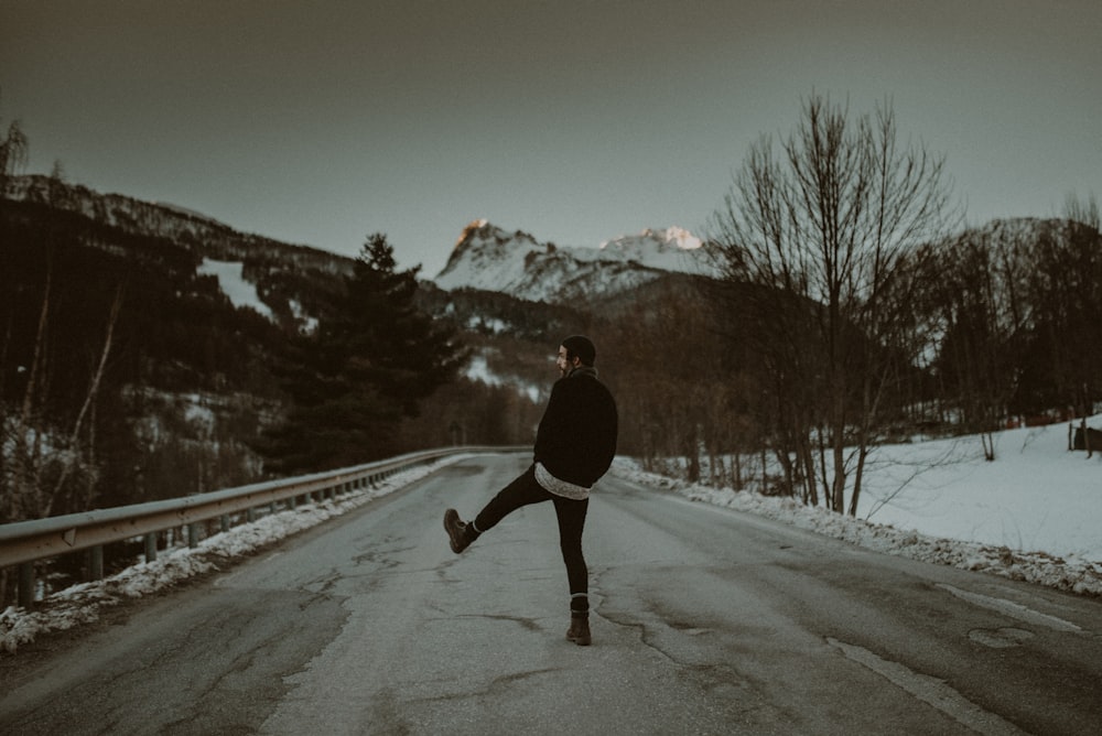 personne en veste noire marchant sur une route enneigée pendant la journée