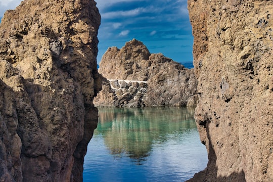 brown rock formation beside blue body of water under blue sky during daytime in Porto Moniz Portugal