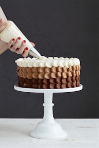 A baker's hands expertly decorating a cake with frosting.