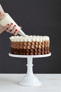 person holding white ice cream cone with brown and white round cake