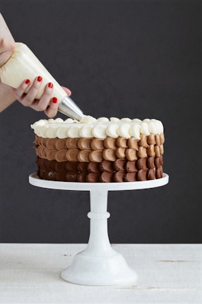 Close-up of hands decorating a chocolate cake with delicate frosting details.