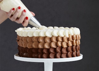 person holding white ice cream cone with brown and white round cake