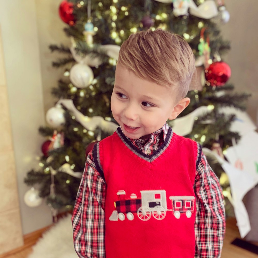 boy in red and white plaid dress shirt standing beside christmas tree