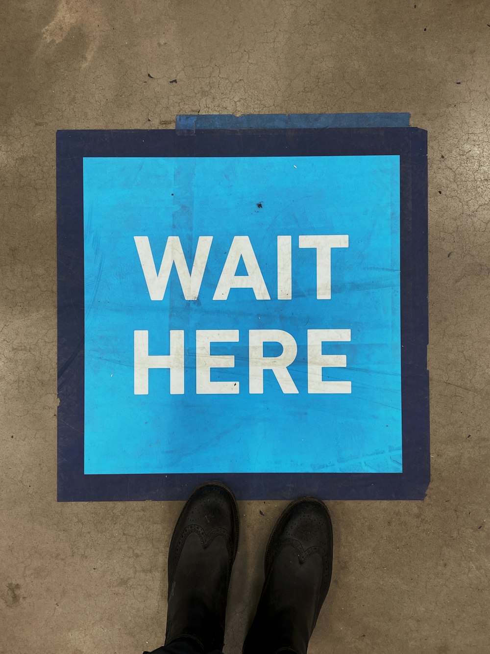 Un letrero azul que dice espera aquí en el piso