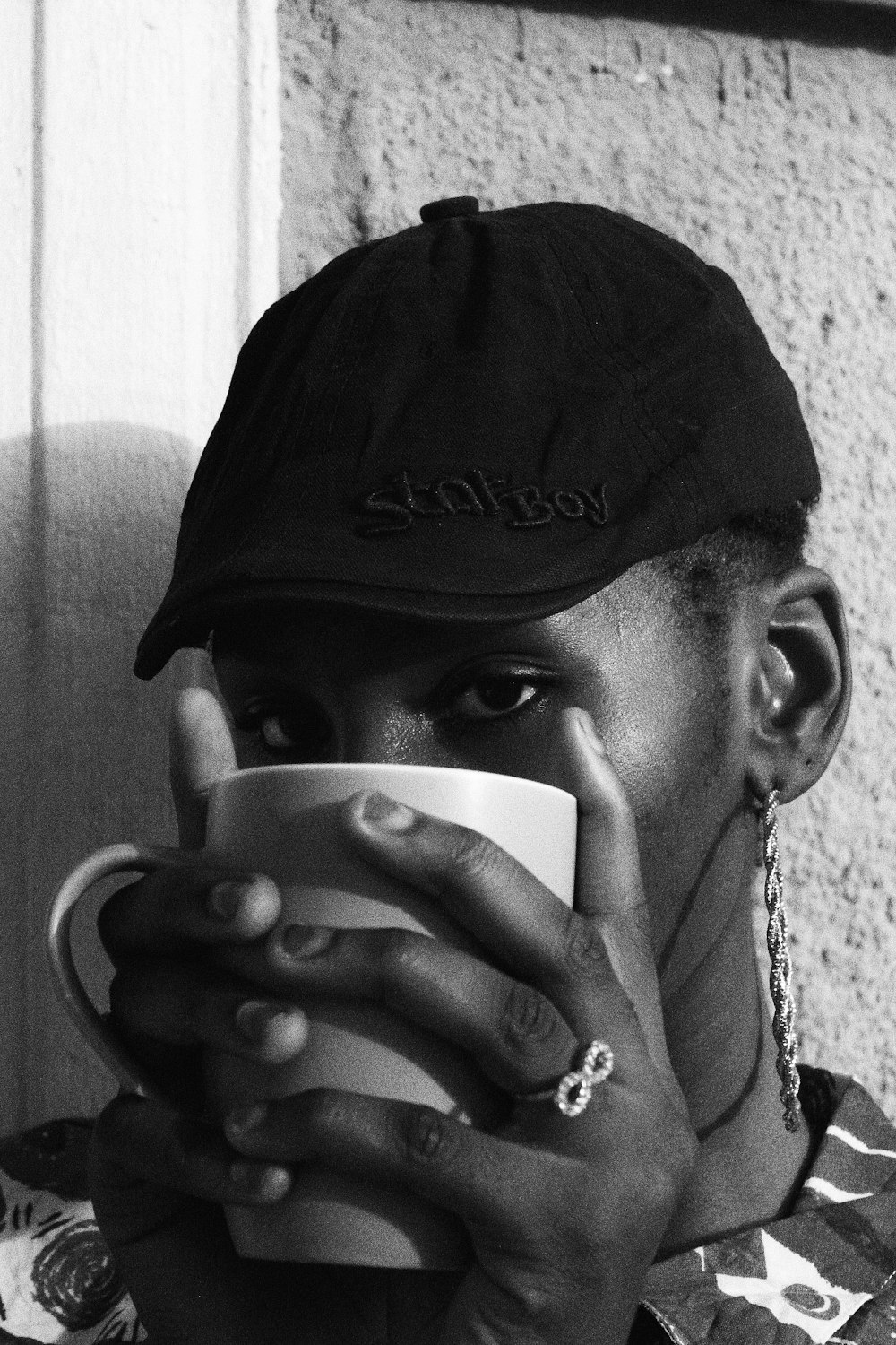 man in black hat and silver necklace holding white ceramic mug